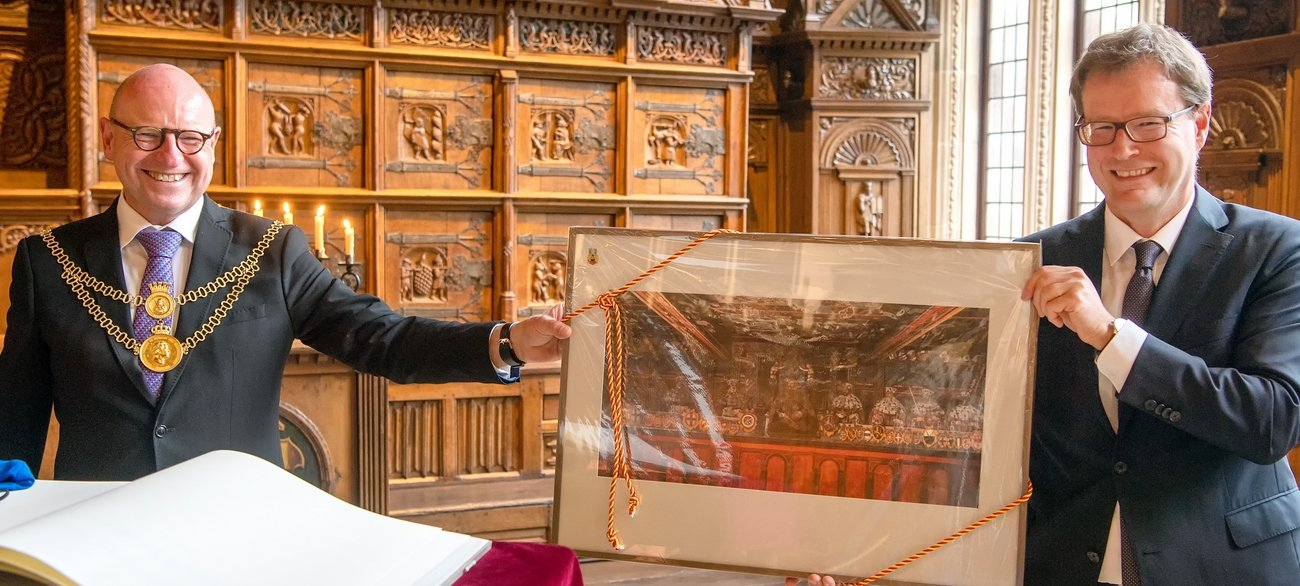 Foto: Geschenk unter Freunden: Oberbürgermeister Markus Lewe freut sich über eine Reproduktion, die Amtskollege Dr. Johannes Bruns aus Thüringen mitgebracht hat. Sie zeigt die Wandmalerei im historischen Mühlhäuser Rathaus. Foto: Presseamt  Münster / Wolfram Linke.