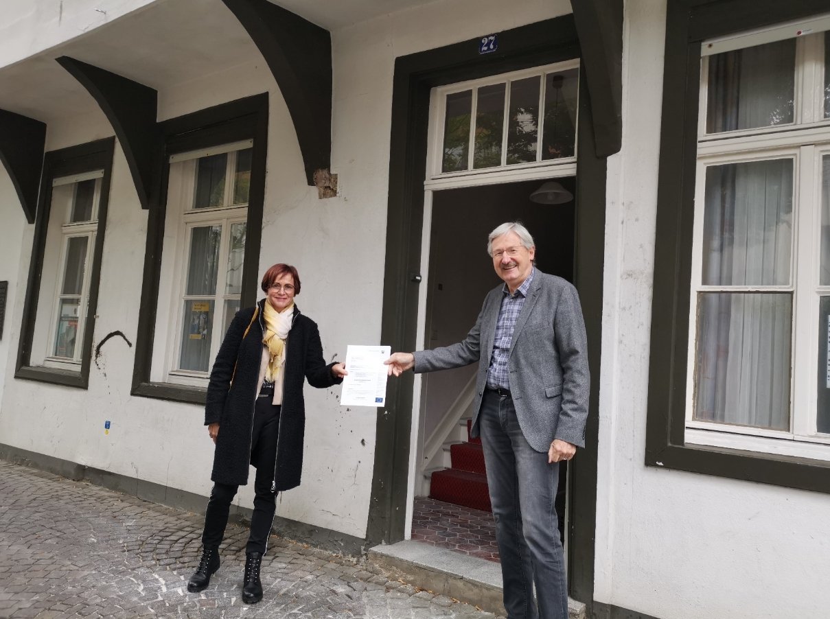 Karin Geißler (l.), Dezernentin für Denkmalschutz und Denkmalpflege bei der Bezirksregierung Münster, überreicht den Bescheid an Dr. Peter Rohlmann (r.), den Vorsitzenden des Vereins Historische Altstadt Rheine e.V. vor dem historischen Traufenhaus an der Münstermauer in Rheine Bildquelle: Reiner Wellmann